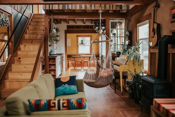 A cozy living room with a wooden staircase, a hanging chair, and a fireplace.