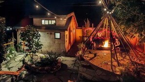 Area esterna ben illuminata con patio in pietra, una tenda e luci decorative appese.