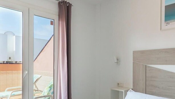 Een hotelkamer met een bed, een raam met gordijnen, uitzicht naar buiten en een klein nachtkastje.