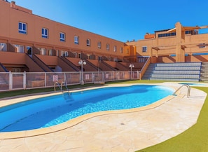 A swimming pool with a stone deck, a staircase leading to a building, and a clear blue sky.