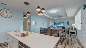 A modern kitchen with a large island, pendant lights, and a dining area with wooden chairs and a table. - 2 Homes- Perfect location for large families or groups. Pool, Walk to BEACH (Port Aransas)