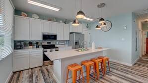 A modern kitchen with white cabinets, a central island with stools, stainless steel appliances, and pendant lighting. - 2 Homes- Perfect location for large families or groups. Pool, Walk to BEACH (Port Aransas)