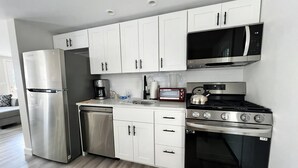 Una cocina moderna con gabinetes blancos, electrodomésticos de acero inoxidable, microondas, tostadora y hervidor.