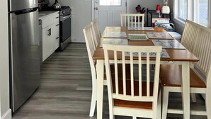 Una cocina moderna con armarios blancos, electrodomésticos de acero inoxidable y una zona de comedor con mesas y sillas de madera.
