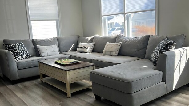 Una sala de estar moderna con un sofá seccional gris, una mesa de centro de madera y un ventanal que proporciona luz natural.