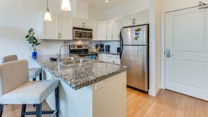 A modern kitchen with white cabinets, a stainless steel refrigerator, a microwave, and a granite countertop. - Stunning Lake View Condo (West Kelowna)