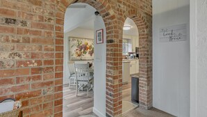 A hallway with brick walls and white doorways leading to a kitchen and dining area. - Redondo Beach Bungalow (Des Moines)