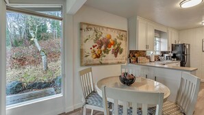 A modern kitchen with white cabinetry, a central island, and a dining area with a round table and chairs. - Redondo Beach Bungalow (Des Moines)
