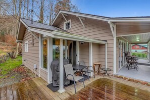 A covered outdoor patio with a table and chairs, a grill, and a view of a red house in the background. - Redondo Beach Bungalow (Des Moines)