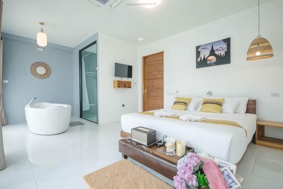 A modern bedroom with a large bed, a white bathtub, and a wooden door.