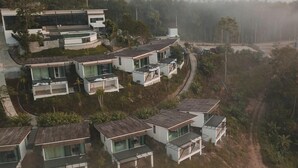 Un quartier résidentiel avec des maisons modernes dotées de grandes fenêtres et de balcons, entouré de collines et baigné d’une atmosphère brumeuse.