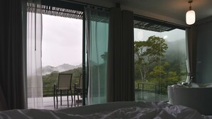 Une chambre avec un grand lit, une chaise et une table près d’une porte-fenêtre coulissante.