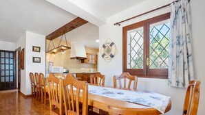 Een eetruimte met een houten tafel en stoelen, een keuken achtergrond en een raam met gordijnen.