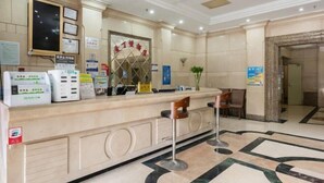 Zona de recepción de un hotel con mostrador, sillas, un espejo grande y un suelo estampado.