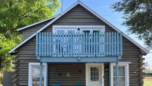 A log cabin with a balcony, two blue Adirondack chairs, a small porch area, and a warning sign about security cameras.
