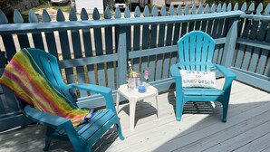 A blue deck with two matching chairs and a small table, a white picket fence, and a clear view of the surrounding area.