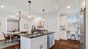 Una cocina moderna con una isla central, armarios blancos, electrodomésticos de acero inoxidable e iluminación colgante.