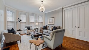 Un salón amplio con un sofá gris, un sillón estampado, una mesa de centro y un candelabro.
