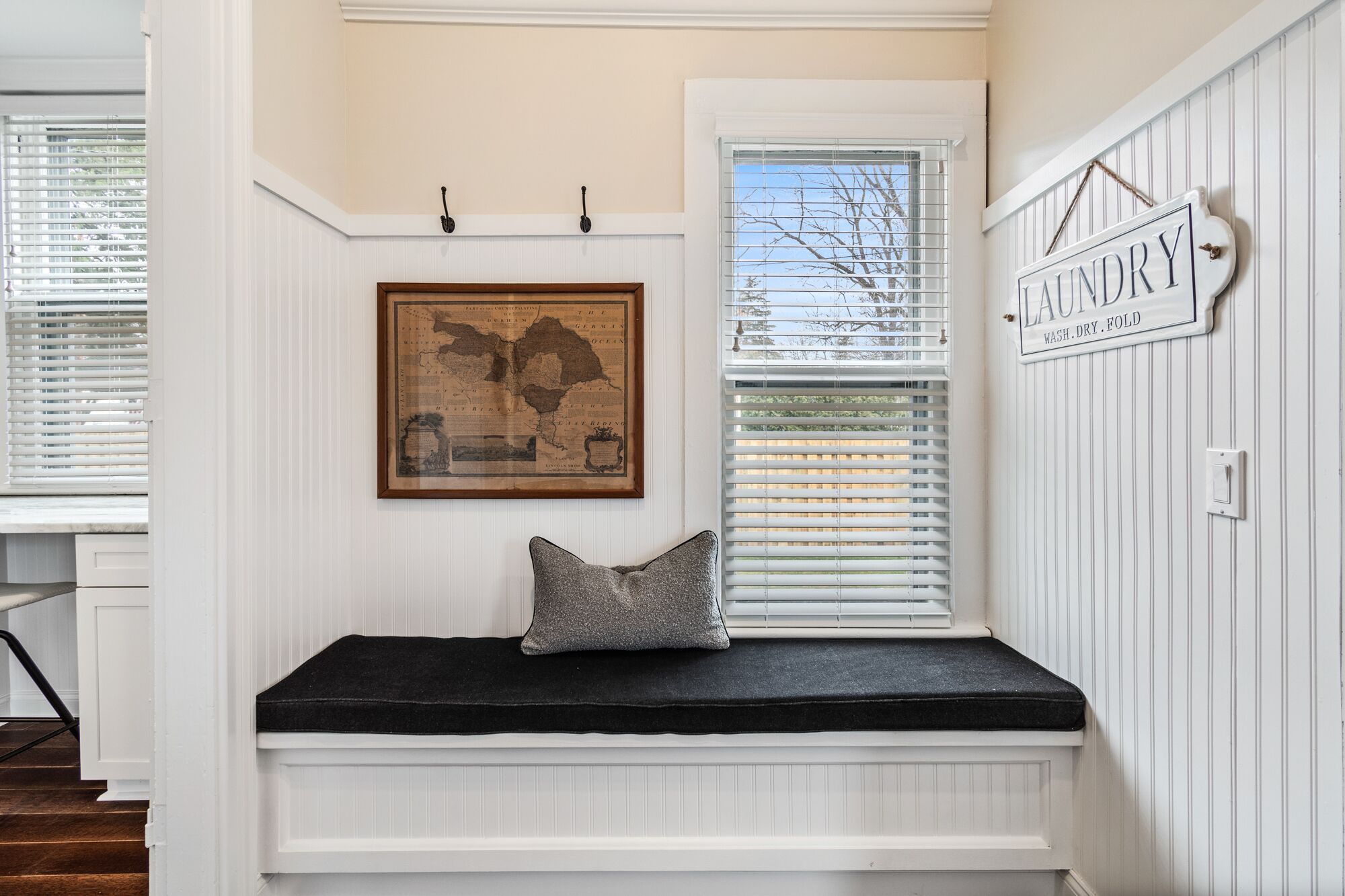 A room with a built-in bench, a map, a window with blinds, and a laundry sign.