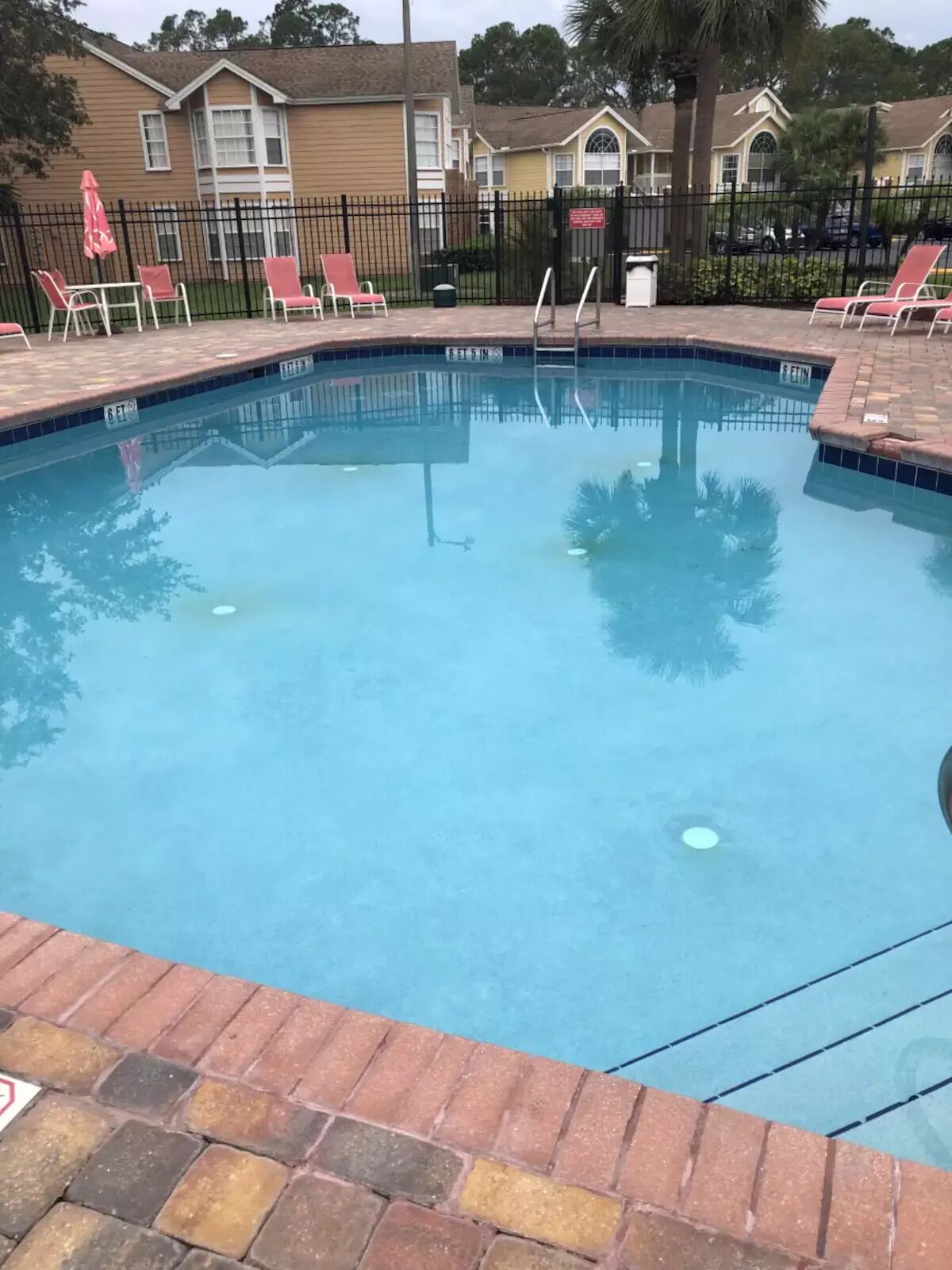 Una piscina con borde de ladrillo, rodeada de sillas de descanso y sombrillas.