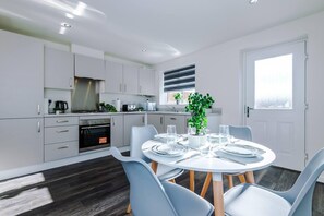 A modern kitchen with white cabinets, a built-in oven, and a dining area with a round table set for four. - Stunning 2-Bed House in Manchester with Canal view (Salford)