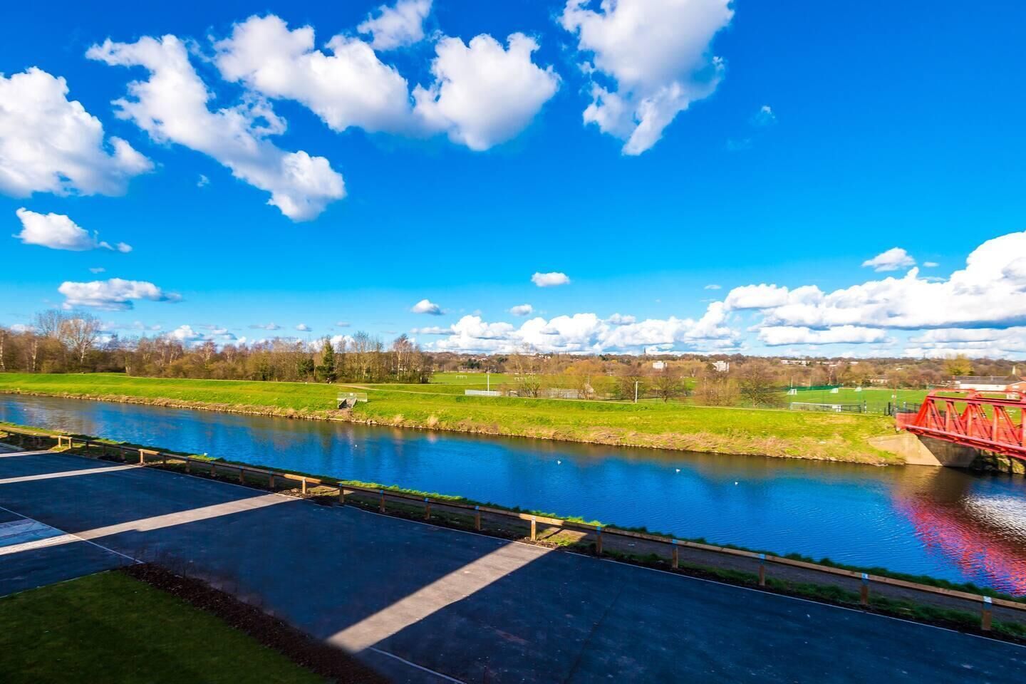 Een rivier met een rode brug, een helder blauwe lucht en groene velden op de achtergrond.