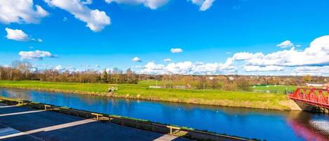 Een rivier met een rode brug, een helder blauwe lucht en groene velden op de achtergrond.