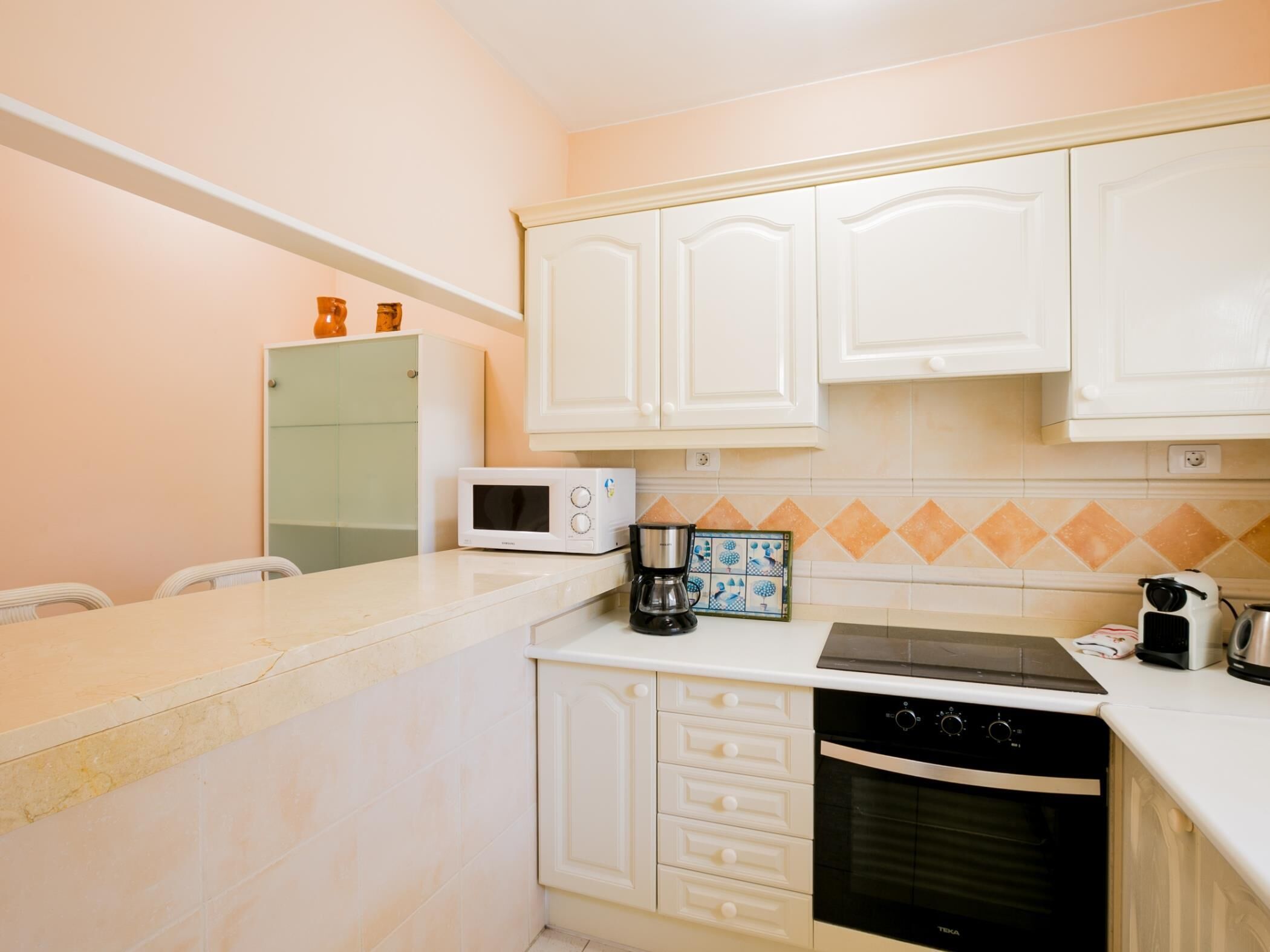A compact kitchen with white cabinets, a microwave, a coffee maker, a stove, and an oven.