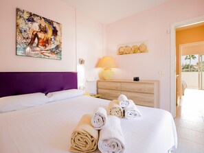 Une chambre d’hôtel avec un lit, une tête de lit, un tableau, une lampe, une commode en bois et une vue sur l’extérieur.