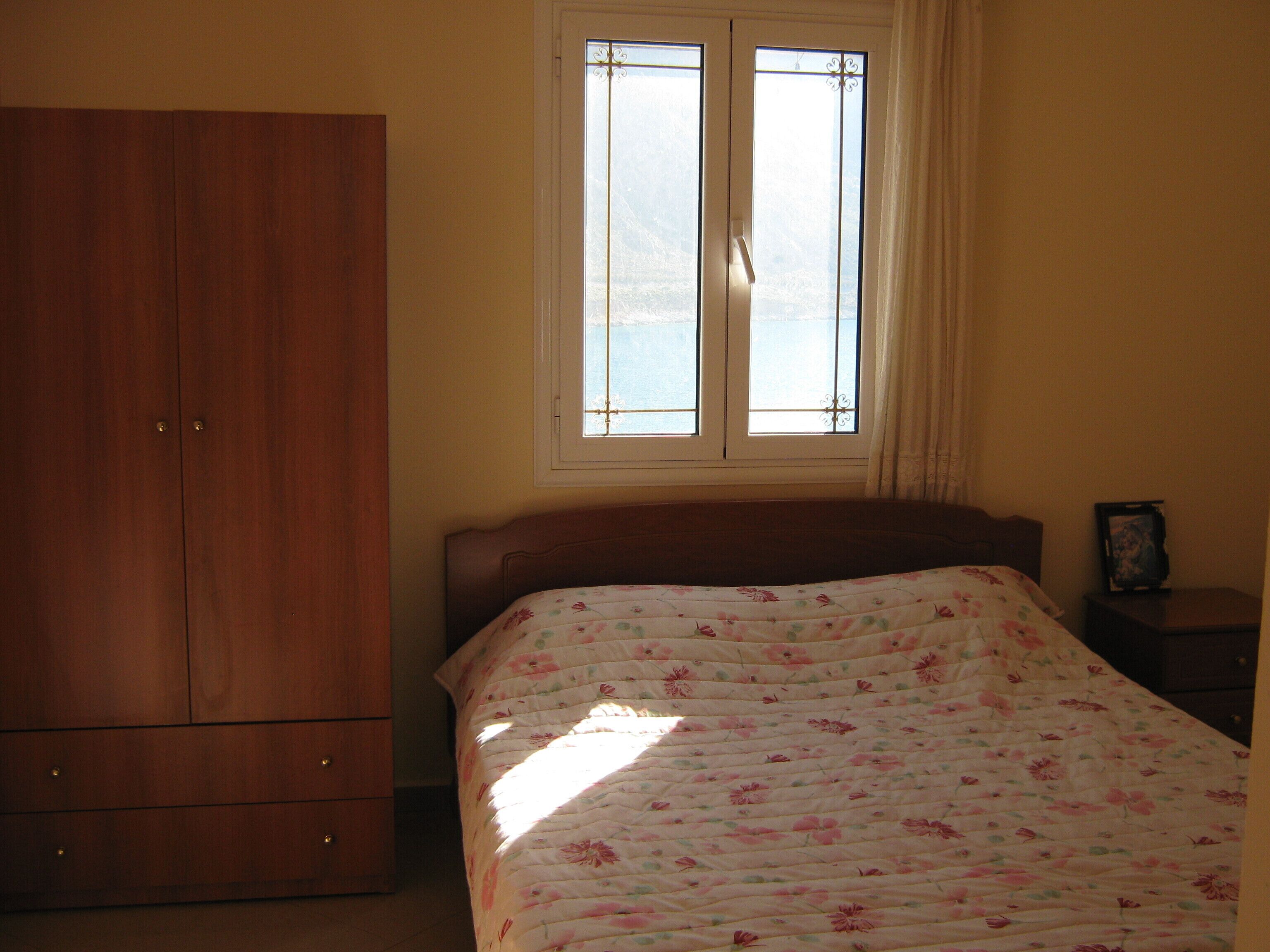 Ein Schlafzimmer mit einem Bett, einem Schrank, einem Fenster und einem Nachttisch.