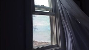 Une fenêtre donnant sur une plage et un ciel nuageux.
