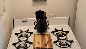 Une cuisinière blanche à quatre brûleurs, une planche à découper en bois et une casserole noire posée sur le brûleur avant.
