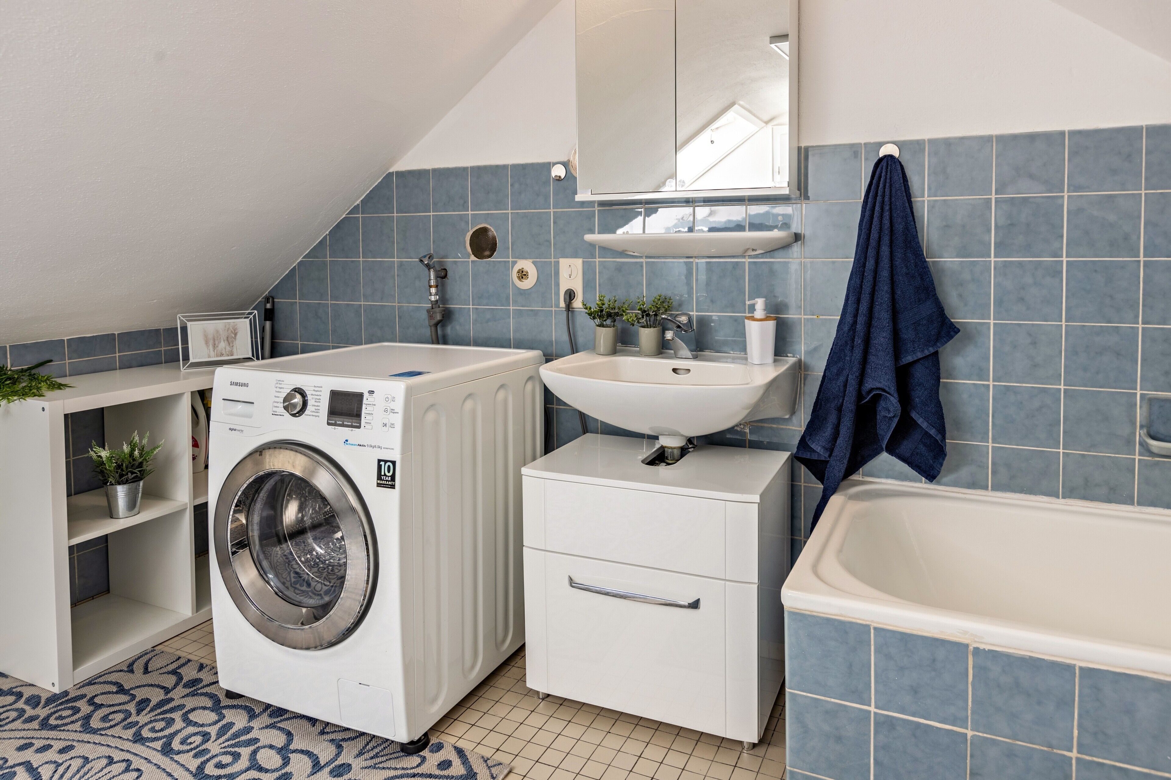 Ein kleines Badezimmer mit Waschmaschine, Waschbecken, Schrank und Badewanne.