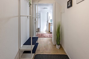 Un couloir avec une porte blanche, un présentoir m étallique, une plante en pot et un tapis rouge.