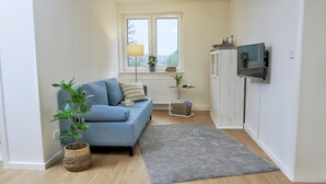 A living room with a sofa, a grey rug, a television, and a window with a plant. - Apartment "Quartier 3" with Wi-Fi (Zeven-Brauel)