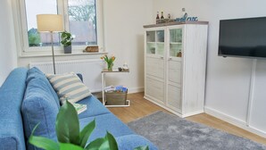 A living room with a sofa, a cabinet, a television, and a window with a view. - Apartment "Quartier 3" with Wi-Fi (Zeven-Brauel)