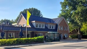 A two-story building with a blue roof, a yellow flag, and a small green gazebo. - Apartment "Quartier 3" with Wi-Fi (Zeven-Brauel)