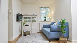 A compact living space with a sofa, a television, a window with a view of trees, a lamp, and a plant.