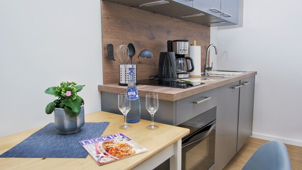 A modern kitchen with a coffee maker, kettle, and a bottle of water. There's a plant on the table and a magazine. - Apartment "Quartier 3" with Wi-Fi (Zeven-Brauel)