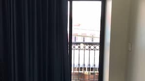 A hotel room with a bed, a curtain, a door leading to a balcony, and a view of buildings outside. - Hotel Chom Chao City (Phnom Penh)