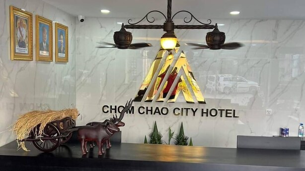 A reception desk with a chandelier, framed pictures, and a decorative horse carriage. - Hotel Chom Chao City (Phnom Penh)