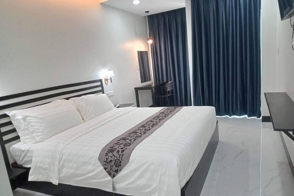Een moderne hotelkamer met een groot bed, nachtkastje, lamp en televisie.