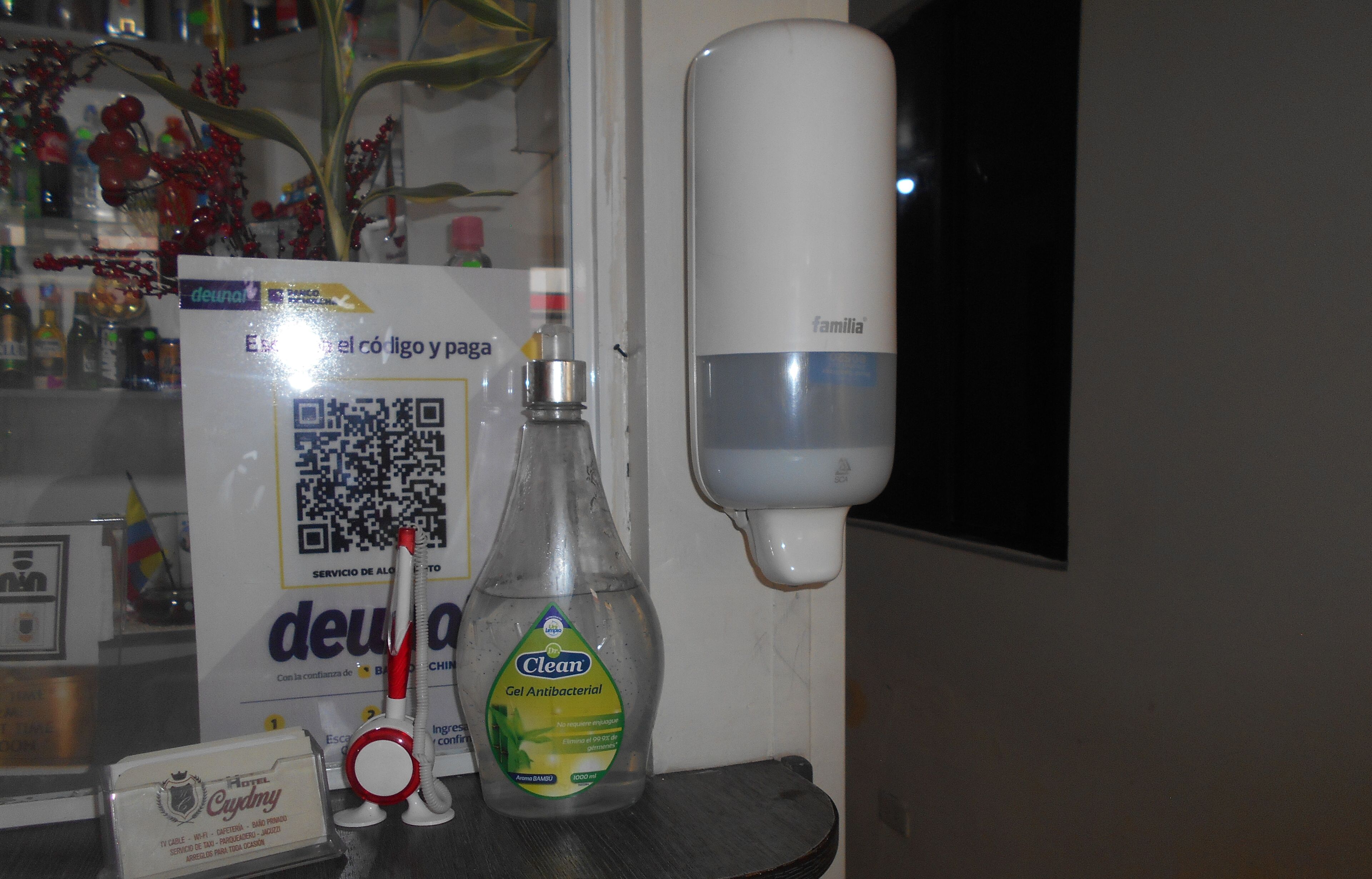 A hotel room with a bottle of 'Clean' gel antibacterial, a hand sanitizer dispenser, and a sign with a QR code.