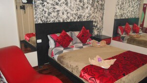 A bedroom with a bed, a red chair, a nightstand, and a mirror.