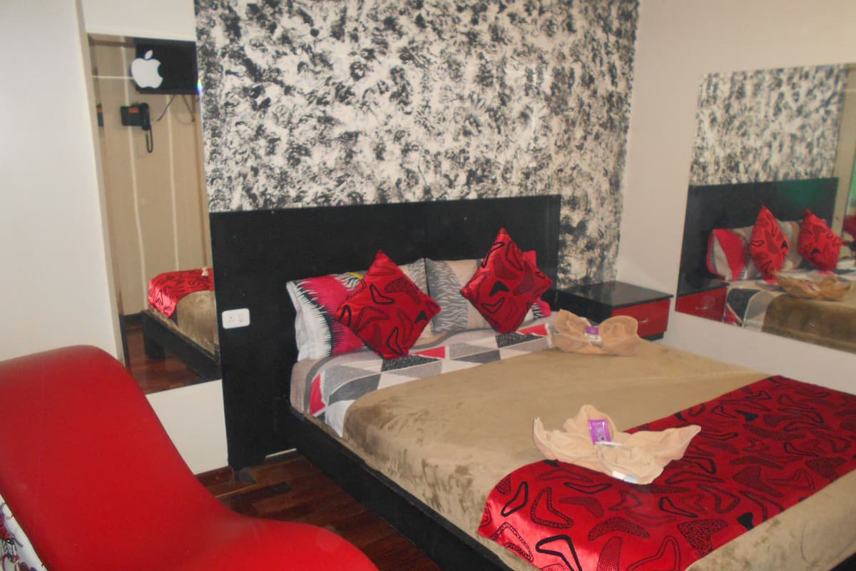A bedroom with a bed, a red chair, a nightstand, and a mirror.