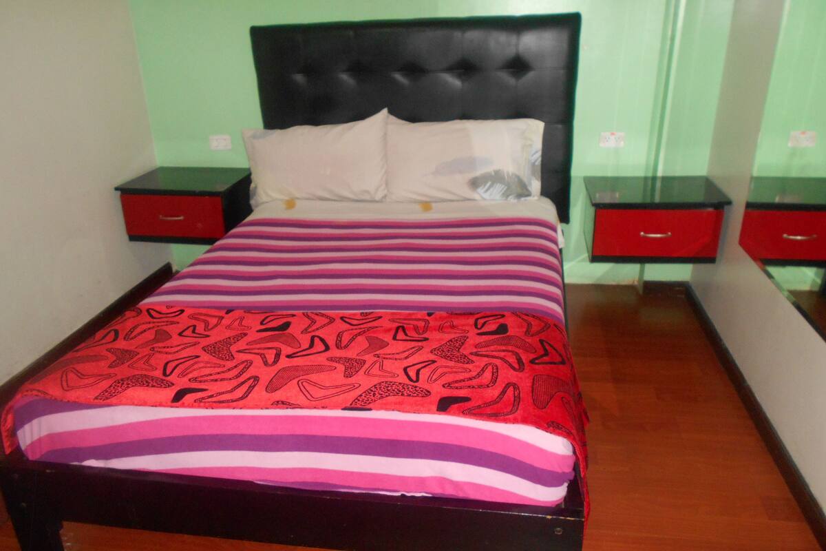 A bed with a patterned bedspread, two bedside tables, and a red drawer unit.