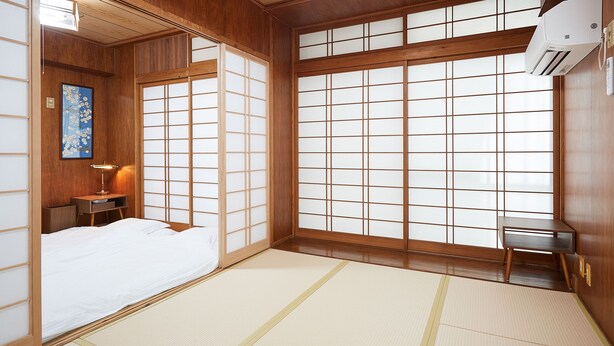 Una habitación japonesa tradicional con suelo de tatami, una cama, un escritorio y puertas correderas.