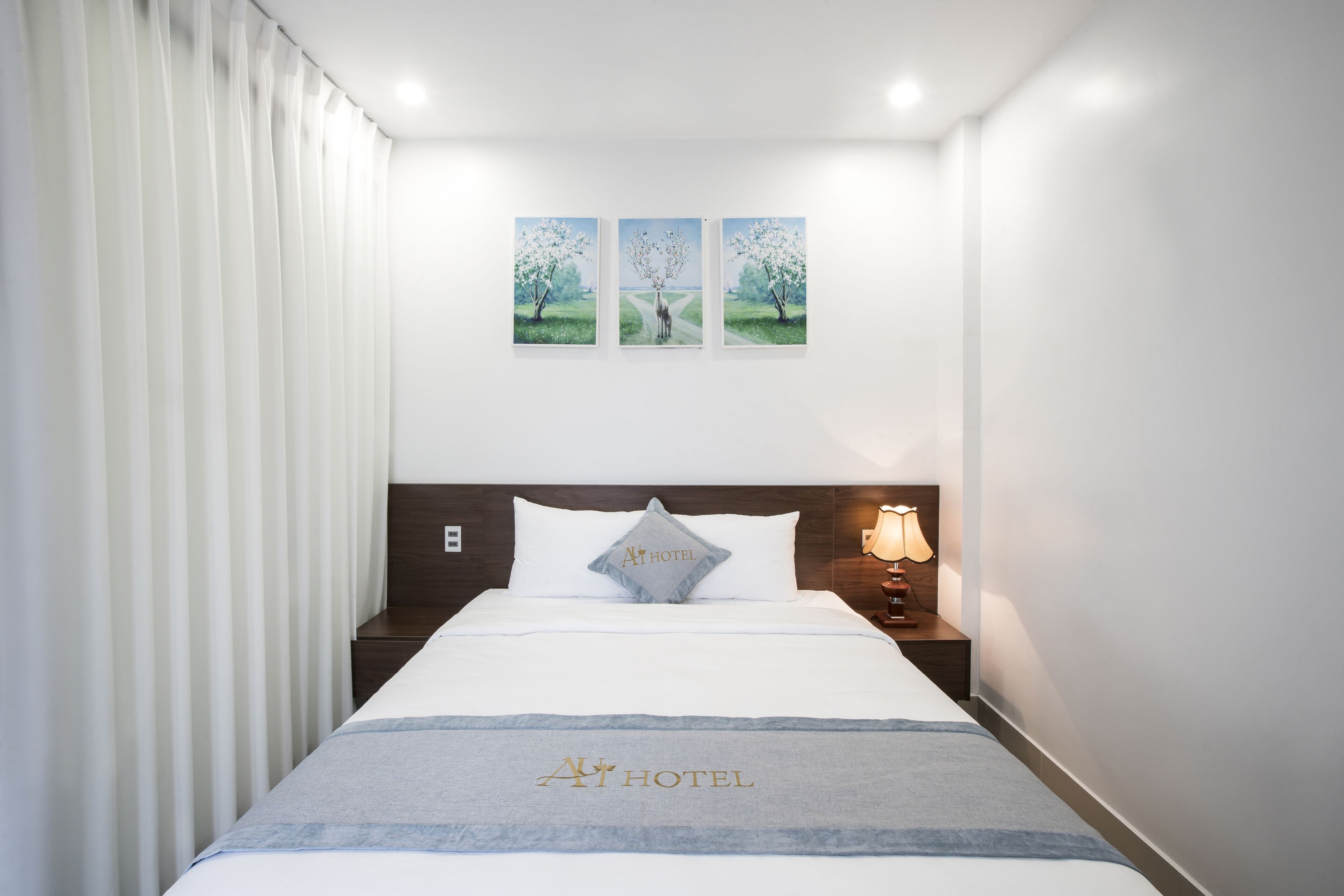 A hotel room with a neatly made bed, a nightstand with a lamp, and three framed pictures on the wall.