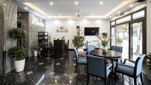 A modern hotel lobby with a marble floor, a reception desk, seating area, and a large window offering a view of the street. - Aui Hotel (Hai Phong)