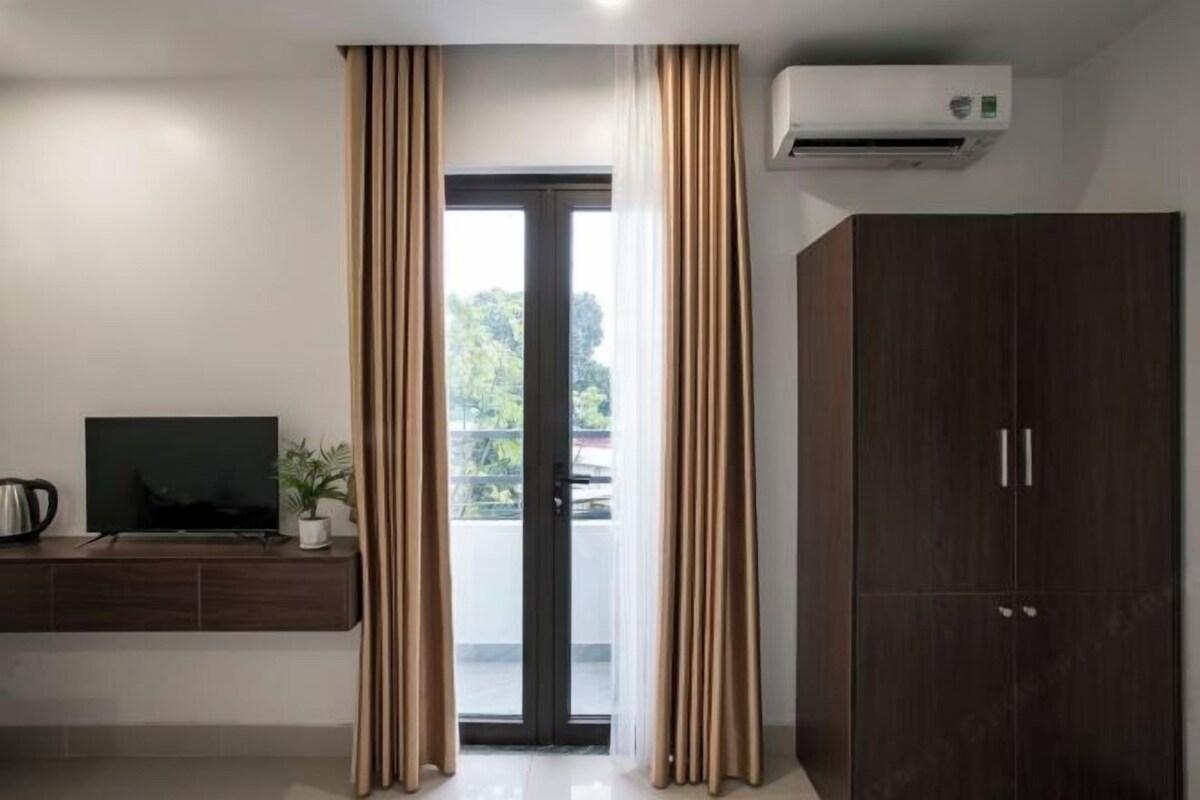 A room with a sliding glass door, a dark wooden wardrobe, a flat-screen TV on a wooden console, and an air conditioning unit on the wall.